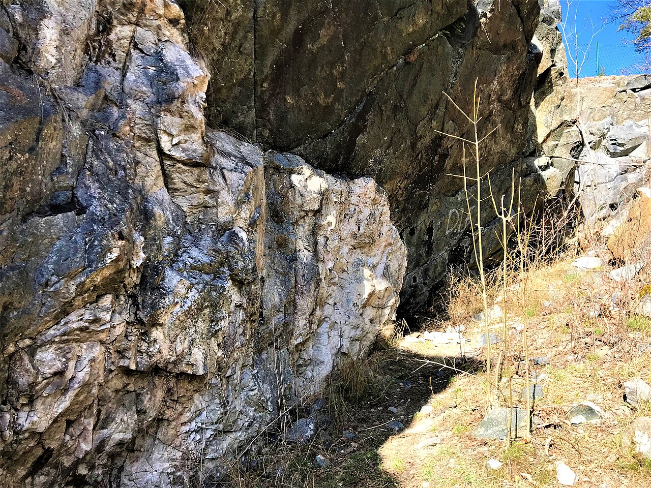 Stenig bergvägg med en grotta eller berghåla omgiven av torr vegetation och gräs.